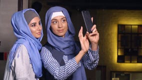 De moderne Moslimvrouwen nemen beelden op een mobiele telefoon Meisjes in en hijabs die spreken glimlachen royalty-vrije stock fotografie De moderne Moslimvrouwen nemen beelden op een mobiele telefoon Meisjes in en hijabs die spreken glimlachen royalty-vrije stock fotografie
