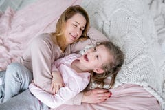 De mooie jonge moeder en haar weinig dochter liggen samen op het bed in de slaapkamer, lachen, koesteren en hebben pret royalty-vrije stock afbeelding De mooie jonge moeder en haar weinig dochter liggen samen op het bed in de slaapkamer, lachen, koesteren en hebben pret royalty-vrije stock afbeelding