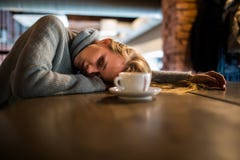 De mooie jonge vrouw ligt op handen, zit bij houten lijst in cafetaria, drinkt koffie Ontspan en rust concept royalty-vrije stock foto De mooie jonge vrouw ligt op handen, zit bij houten lijst in cafetaria, drinkt koffie Ontspan en rust concept royalty-vrije stock foto