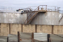 De oude tanks van de metaal industriële opslag met roestige die inspectieladders en de kleppen door een golfstaal worden omringd royalty-vrije stock foto De oude tanks van de metaal industriële opslag met roestige die inspectieladders en de kleppen door een golfstaal worden omringd royalty-vrije stock foto