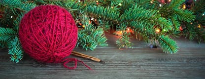 De rode bal van het wolgaren en houten breinaalden dichtbij de groene boom van het Kerstmisbont en heldere kleurrijke lichten op royalty-vrije stock afbeelding De rode bal van het wolgaren en houten breinaalden dichtbij de groene boom van het Kerstmisbont en heldere kleurrijke lichten op royalty-vrije stock afbeelding