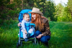 De roodharige jonge glimlachende grootmoeder loopt met haar twee-jaar-oude kleinzoon in de zomer in het bos stock afbeelding De roodharige jonge glimlachende grootmoeder loopt met haar twee-jaar-oude kleinzoon in de zomer in het bos stock afbeelding