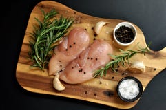 De ruwe verse ongekookte schotel van de het vleesfilet van de kippenborst met rozemarijn, peper, zout en knoflook op houten raad stock afbeeldingen De ruwe verse ongekookte schotel van de het vleesfilet van de kippenborst met rozemarijn, peper, zout en knoflook op houten raad stock afbeeldingen