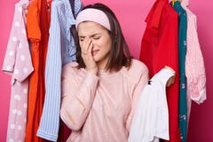De schreeuwende vrouw houdt rechtse dichtbijgelegen haar gezicht, houdt hanger met wit overhemd terwijl status bij haar garderobe stock foto De schreeuwende vrouw houdt rechtse dichtbijgelegen haar gezicht, houdt hanger met wit overhemd terwijl status bij haar garderobe stock foto