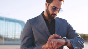 De succesvolle gebaarde mens in zonnebril regelt de tijd via slim horloge terwijl het lopen door de luchthaventerminal stock videobeelden De succesvolle gebaarde mens in zonnebril regelt de tijd via slim horloge terwijl het lopen door de luchthaventerminal stock videobeelden