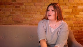 De te zware vrouwelijke student het letten op verschrikkingsfilm op TV wordt geschokt en krast haar hoofd in comfortabele huisatm stock videobeelden De te zware vrouwelijke student het letten op verschrikkingsfilm op TV wordt geschokt en krast haar hoofd in comfortabele huisatm stock videobeelden