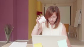 De teleurgestelde vrouw zit voor laptop, drinkt water en giet water op overlappingsbovenkant stock video De teleurgestelde vrouw zit voor laptop, drinkt water en giet water op overlappingsbovenkant stock video
