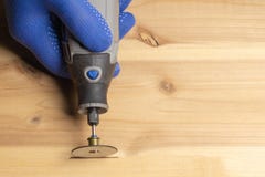 De timmerman in blauwe beschermende handschoenen behandelt houten dremel stock fotografie De timmerman in blauwe beschermende handschoenen behandelt houten dremel stock fotografie