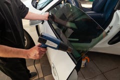 De tovenaar voor het installeren van extra materiaal plakt een tintfilm op het zij voorglas van de auto en droogt het glas met stock foto De tovenaar voor het installeren van extra materiaal plakt een tintfilm op het zij voorglas van de auto en droogt het glas met stock foto