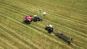 De tractor verzamelt hooi van de gebiedsmening van de hommel stock afbeelding De tractor verzamelt hooi van de gebiedsmening van de hommel stock afbeelding