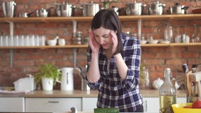 De vrouw in een overhemd met een slechte hoofdpijn in de keuken snijdt groenten stock footage De vrouw in een overhemd met een slechte hoofdpijn in de keuken snijdt groenten stock footage