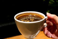 De vrouwelijke Hand die van ` s een Kop van Hete Koffie in de Warme Verlichtings Donkere Zaal houden stock afbeeldingen De vrouwelijke Hand die van ` s een Kop van Hete Koffie in de Warme Verlichtings Donkere Zaal houden stock afbeeldingen