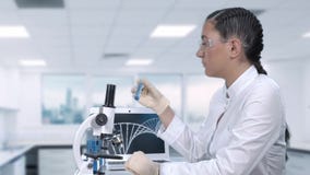 De vrouwelijke laboratoriummedewerker voert laboratoriumtests van een blauwe vloeistof in een reageerbuis uit Wetenschappelijk la stock footage De vrouwelijke laboratoriummedewerker voert laboratoriumtests van een blauwe vloeistof in een reageerbuis uit Wetenschappelijk la stock footage