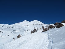 De weg die naar snowcat gaat en toeristen op de achtergrond van het dubbel-geleide onderstel Elbrus neemt royalty-vrije stock afbeelding De weg die naar snowcat gaat en toeristen op de achtergrond van het dubbel-geleide onderstel Elbrus neemt royalty-vrije stock afbeelding