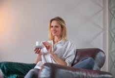 De zitting van de blondevrouw in de leunstoel met koffie royalty-vrije stock afbeelding De zitting van de blondevrouw in de leunstoel met koffie royalty-vrije stock afbeelding