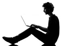 De zitting van het jonge mensensilhouet gegevensverwerkingslaptop royalty-vrije stock fotografie De zitting van het jonge mensensilhouet gegevensverwerkingslaptop royalty-vrije stock fotografie