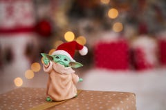 Dec, 2020: Display of Baby Yoda, an action figures, standing in a red cap on christmas background. Bokeh effect.