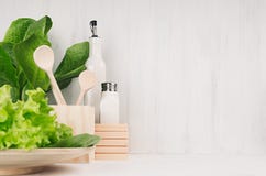 Decoración moderna blanca de la cocina con el plato de madera natural beige, utensilios, ensalada verde fresca en el fondo de mad foto de archivo libre de regalías Decoración moderna blanca de la cocina con el plato de madera natural beige, utensilios, ensalada verde fresca en el fondo de mad foto de archivo libre de regalías