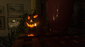 Decorative Halloween pumpkin statue lit with candle glowing in the dark on the shelf in living room