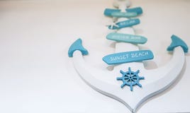 Decorazione bianca dell'ancora che appende su una parete bianca in una casa con i segni blu pastelli della ruota e della spiaggia fotografia stock Decorazione bianca dell'ancora che appende su una parete bianca in una casa con i segni blu pastelli della ruota e della spiaggia fotografia stock