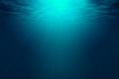 Deep blue sea with rays of sunlight, ocean surface seen from underwater.