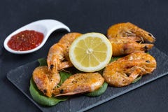 Delicious fresh shrimps cooked, sauteed, with spicy tomato sauce, butter and lime on, served on a black fancy plate. Negative spac