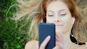Den attraktiva unga kvinnan ligger på gräs, tycker om smartphonen Hår ligger beautifully på gräsmattan arkivbild Den attraktiva unga kvinnan ligger på gräs, tycker om smartphonen Hår ligger beautifully på gräsmattan arkivbild