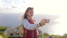 Den blonda flickan gör selfie på bakgrunden av att förbluffa naturen, vaggar, havet, grönska Den långhåriga tonåriga flickan ler lager videofilmer Den blonda flickan gör selfie på bakgrunden av att förbluffa naturen, vaggar, havet, grönska Den långhåriga tonåriga flickan ler lager videofilmer