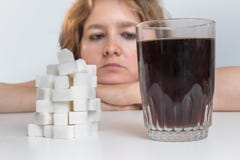 Den diabetiska kvinnan ser på exponeringsglas med coladrinken och högen av socker äta för begrepp som är sjukligt arkivbild Den diabetiska kvinnan ser på exponeringsglas med coladrinken och högen av socker äta för begrepp som är sjukligt arkivbild