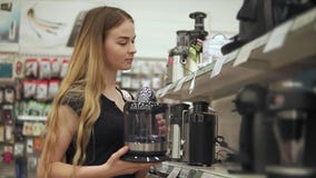 Den ensamma unga kvinnan jämför modellen av kaffemaskiner i en maskinvara shoppar stock video Den ensamma unga kvinnan jämför modellen av kaffemaskiner i en maskinvara shoppar stock video