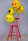 Den gråa lägenhetstudion med stol, tegelstenväggen, guling specificerar röd stol för ballongemojien royaltyfri foto Den gråa lägenhetstudion med stol, tegelstenväggen, guling specificerar röd stol för ballongemojien royaltyfri foto