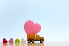 Den gula leksaklastbilen bär på rosa hjärta och många färgrika hjärtor på blå bakgrund arkivbilder Den gula leksaklastbilen bär på rosa hjärta och många färgrika hjärtor på blå bakgrund arkivbilder
