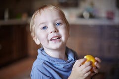 Den gulliga caucasian pysen med blåa ögon och blont hår äter det gula äpplet och att rymma det på händerna som ler royaltyfria bilder Den gulliga caucasian pysen med blåa ögon och blont hår äter det gula äpplet och att rymma det på händerna som ler royaltyfria bilder