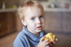 Den gulliga caucasian pysen med blåa ögon och blont hår äter det gula äpplet som rymmer det på händerna royaltyfria bilder Den gulliga caucasian pysen med blåa ögon och blont hår äter det gula äpplet som rymmer det på händerna royaltyfria bilder