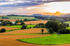 Den härliga solnedgången över bygdlandskap av Rolling Hills med solen strålar genomträngande himmel och belysningbacken Arkivfoton Den härliga solnedgången över bygdlandskap av Rolling Hills med solen strålar genomträngande himmel och belysningbacken Arkivfoton