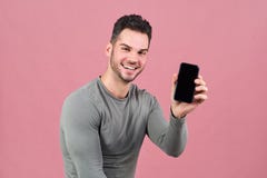Den idrotts- attraktiva mannen i åtsittande t-skjorta breda leenden lyckligt och att rymma i handsmartphone med skärm vände till royaltyfria foton Den idrotts- attraktiva mannen i åtsittande t-skjorta breda leenden lyckligt och att rymma i handsmartphone med skärm vände till royaltyfria foton