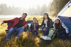 Den lyckliga familjen på en campa tur sitter av tältet som ser till kameran arkivfoto Den lyckliga familjen på en campa tur sitter av tältet som ser till kameran arkivfoto