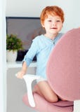 Den lyckliga rödhåriga mannen som lilla barnet behandla som ett barn pojken, sitter i regeringsställning stol på arbetsplatsen royaltyfri fotografi Den lyckliga rödhåriga mannen som lilla barnet behandla som ett barn pojken, sitter i regeringsställning stol på arbetsplatsen royaltyfri fotografi