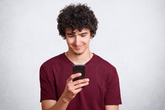 Den lyckliga tonåringen ser gladfully på mobiltelefonen, surfessamkvämnätverk och sikter hans foto med vänner, förbindelse till r royaltyfri fotografi Den lyckliga tonåringen ser gladfully på mobiltelefonen, surfessamkvämnätverk och sikter hans foto med vänner, förbindelse till r royaltyfri fotografi