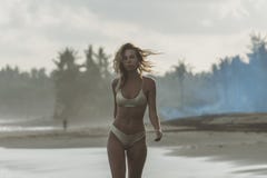 Den långbenta modellen i den vita bikinin är på havstranden som går på havvatten royaltyfria bilder Den långbenta modellen i den vita bikinin är på havstranden som går på havvatten royaltyfria bilder