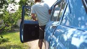 Den oigenkännliga manöppningsdörren och får in i hans gamla retro bil på bygd Ung grabb i hatten som går att köra på hans arkivfilmer Den oigenkännliga manöppningsdörren och får in i hans gamla retro bil på bygd Ung grabb i hatten som går att köra på hans arkivfilmer