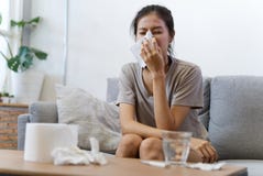 Den sjuka asiatiska unga kvinnan nyser hemma p? soffan med en f?rkylning royaltyfria foton Den sjuka asiatiska unga kvinnan nyser hemma p? soffan med en f?rkylning royaltyfria foton
