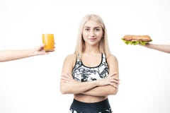 Den sportiga blondinen rymmer i hennes hand en hamburgare och ett exponeringsglas av ny fruktsaft arkivfoton Den sportiga blondinen rymmer i hennes hand en hamburgare och ett exponeringsglas av ny fruktsaft arkivfoton