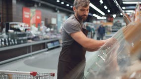 Den stiliga arbetaren av stormarknaden tar munkar från shoppingvagnen och sätter dem i behållare på hyllor in arkivfilmer Den stiliga arbetaren av stormarknaden tar munkar från shoppingvagnen och sätter dem i behållare på hyllor in arkivfilmer