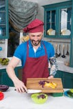 Den stiliga le kocken med den tatuerade handen rymmer skärbrädan med paprika och kål Kocken sätter paprika in i den gula plattan royaltyfria foton Den stiliga le kocken med den tatuerade handen rymmer skärbrädan med paprika och kål Kocken sätter paprika in i den gula plattan royaltyfria foton