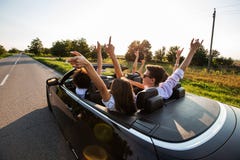 Den svarta cabrioleten är på landsvägen Den lyckliga gruppen av unga flickor och grabbar sitter i bilen rymmer upp deras händer arkivfoto Den svarta cabrioleten är på landsvägen Den lyckliga gruppen av unga flickor och grabbar sitter i bilen rymmer upp deras händer arkivfoto