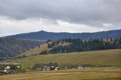 Den tunga gr? f?rgen f?rdunklar i den kalla h?sthimlen ?ver by med sm? hus som ?r l?ngv?ga i bergen och f?lten lopp folk royaltyfri fotografi Den tunga gr? f?rgen f?rdunklar i den kalla h?sthimlen ?ver by med sm? hus som ?r l?ngv?ga i bergen och f?lten lopp folk royaltyfri fotografi