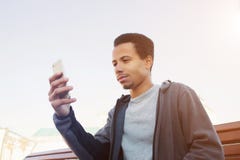 Den unga afro- amerikanska mannen i sportkläder använder smartphonen arkivbilder Den unga afro- amerikanska mannen i sportkläder använder smartphonen arkivbilder