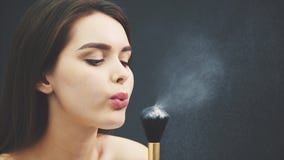 Den unga kvinnan blåser på ett borstepulver för att utgöra makeup Kantjusterad bild Makeupapplikation i närbild Isolerat p? a arkivfilmer Den unga kvinnan blåser på ett borstepulver för att utgöra makeup Kantjusterad bild Makeupapplikation i närbild Isolerat p? a arkivfilmer