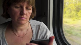 Den unga kvinnan n?ra f?nstret av ett r?rande drev meddelar vid telefonen Den unga kvinnan n?ra f?nstret av ett r?rande drev meddelar vid telefonen